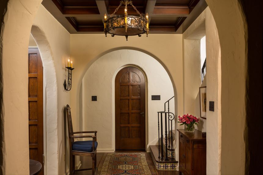 这个小而舒适的门厅有拱形的入口，与拱形木门和支撑着深棕色枝形吊灯的木质方格天花板相匹配。这与深色硬木地板搭配得很好，地板上主要覆盖着彩色图案的区域地毯。