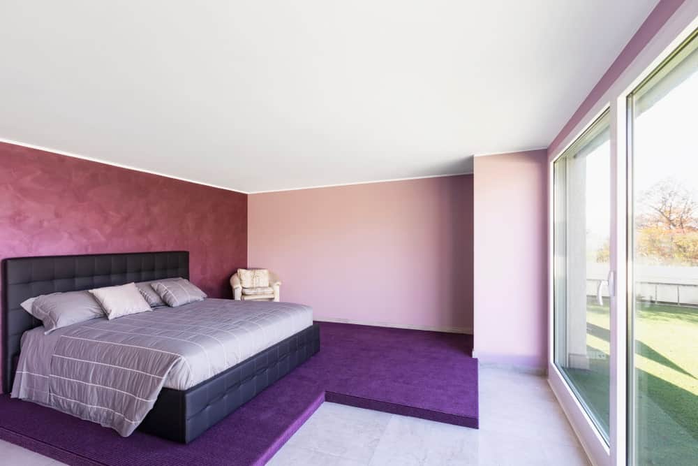 主卧室，现代舒适的床设置在紫色地板上。这个房间还有一扇门，直接通往这栋房子的后院。