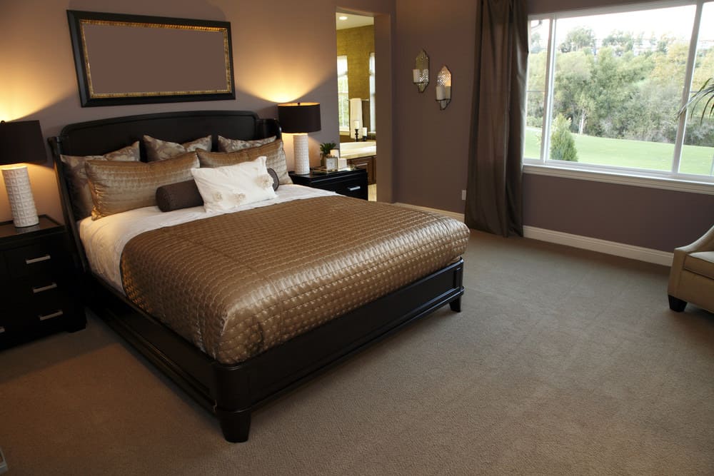 一个集中的镜头在这个主卧室的优雅的床设置围绕着紫色的墙壁和地毯地板。这个房间还有自己的浴室。