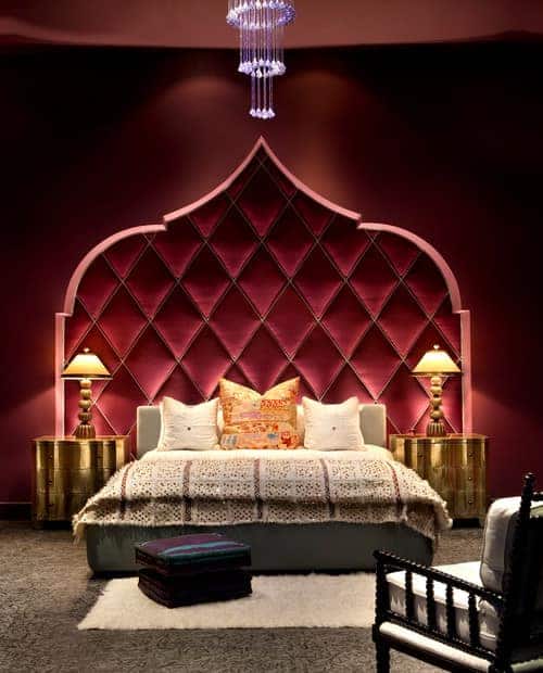 一个集中的镜头在这个主卧室的豪华床设置，两边有优雅的镀金床头柜，顶部有优雅的台灯。房间的特色是红墙和地毯地板。