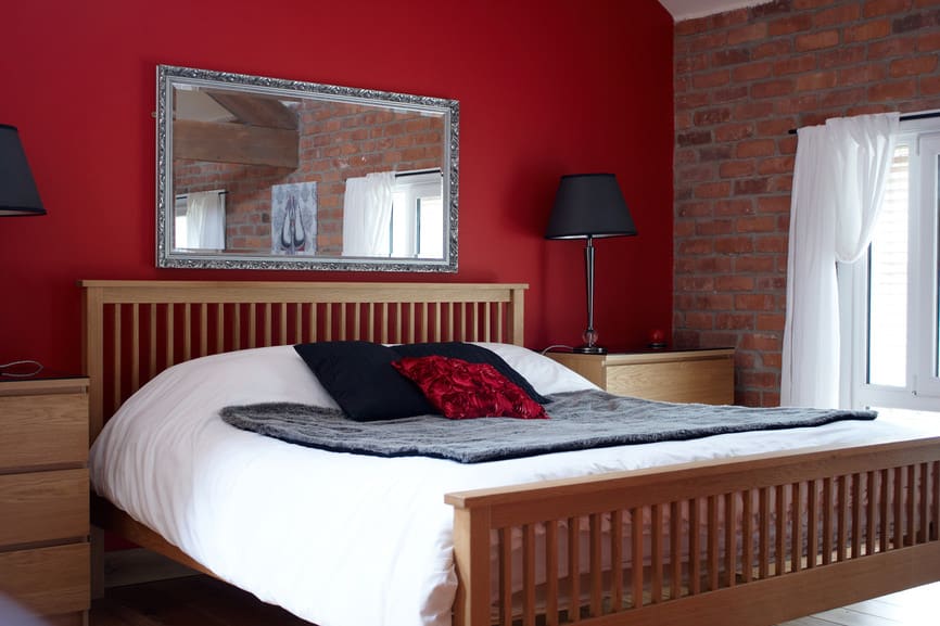 这张照片聚焦在主卧室的大床上，床上有一个木制的框架，两边都有黑色的台灯。房间的特点是混凝土红墙和红砖墙。