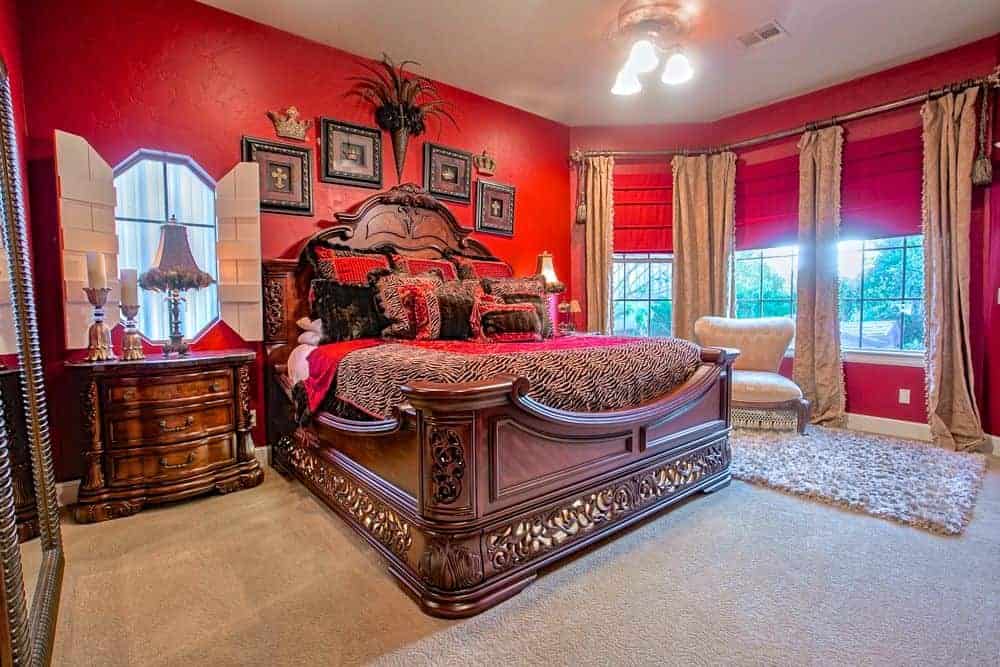 一个中型的主卧室拥有一个大的优雅的床被红墙和地毯地板包围。