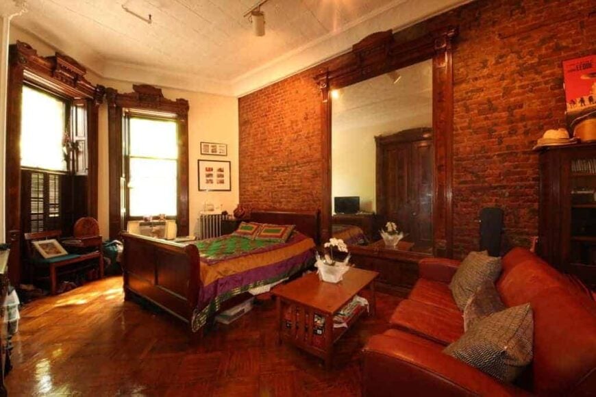 主卧室设有时尚的地板和红砖墙。房间里有一张漂亮的双人床，旁边有一张棕色的皮沙发。