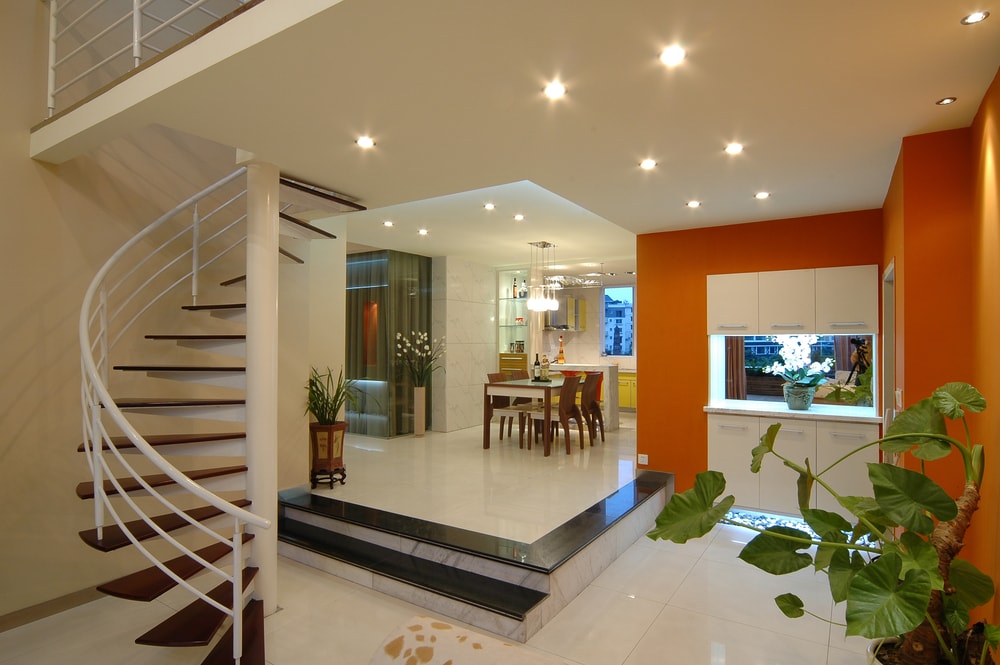 一座现代化的房子，以瓷砖地板和白色和橙色的墙壁为特色，白色的天花板由嵌入式灯照亮。该住宅还设有旋转楼梯。