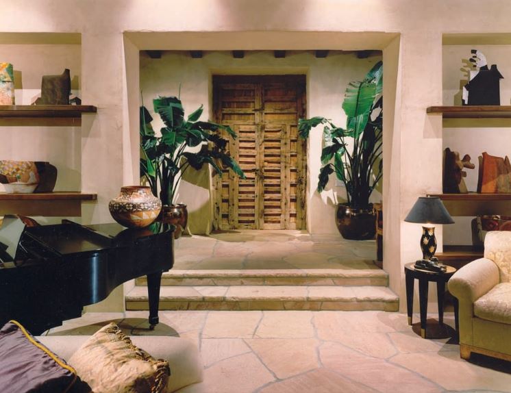 这两盆盆栽在灰白色的墙壁上格外显眼，因为它们位于设计独特的木门两侧。这间西南风格的门厅与这栋房屋的其他部分一样，铺着不规则的石头地板，入口处有一架三角钢琴。