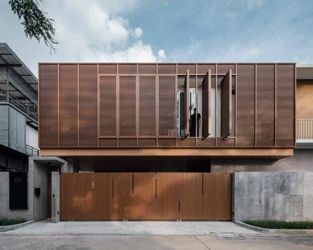 这是房子的正面外观，地面层的车库门上有一致的深色木质色调，上层的板条面板上有一些可以旋转的面板，可以打开内部。
