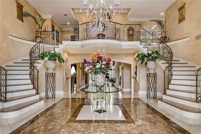 宏伟的门厅有华丽的大理石地板搭配圆形玻璃顶中心桌，复杂的枝形吊灯，和花基座坐在优雅的分叉楼梯。