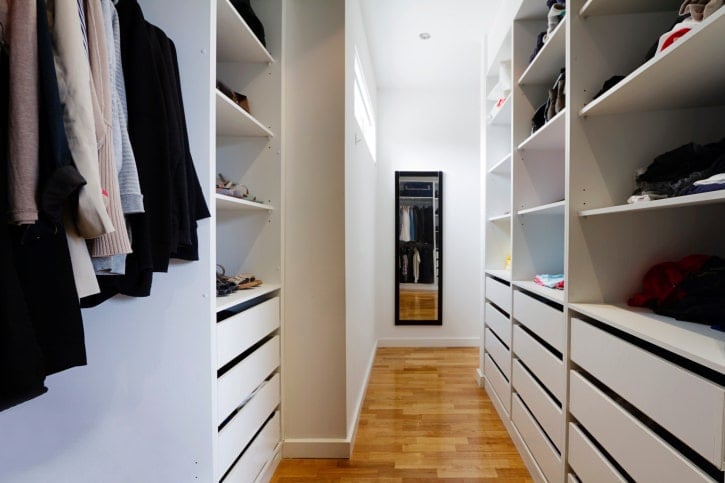 极简主义步入式衣柜拥有丰富的硬木地板和白色橱柜，与黑色镜框镜子形成对比，与墙壁融为一体。