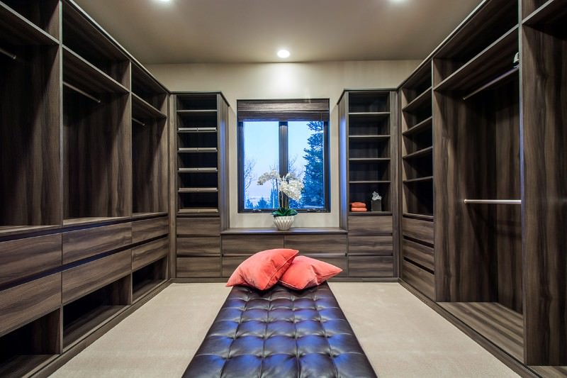 黑色簇绒脚垫上的珊瑚枕头在步入式衣柜中脱颖而出，展示木质模块化橱柜和覆盖柳条卷帘的铝框窗户。