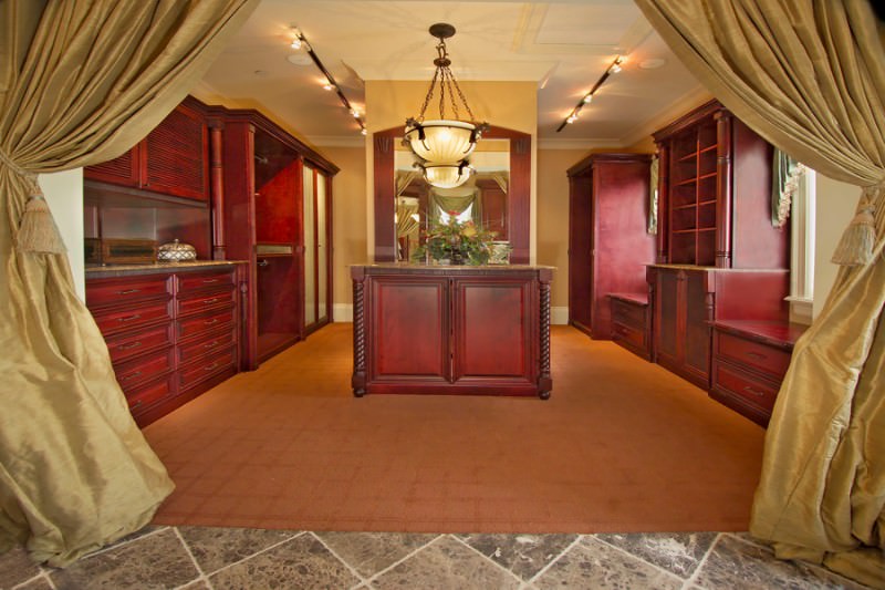 通过金色窗帘，可以看到步入式衣柜，红木橱柜和位于墙镜对面的匹配岛。它由一个玻璃圆顶吊坠和黑色轨道灯照明。