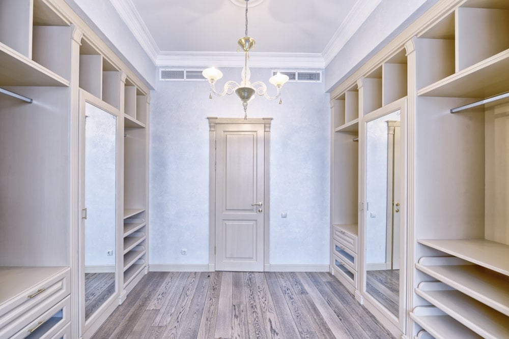 带镜面门的轻木橱柜在这个步入式衣柜中增添了完美的对称，天然硬木地板和一个可爱的玻璃枝形吊灯悬挂在普通的白色天花板上。