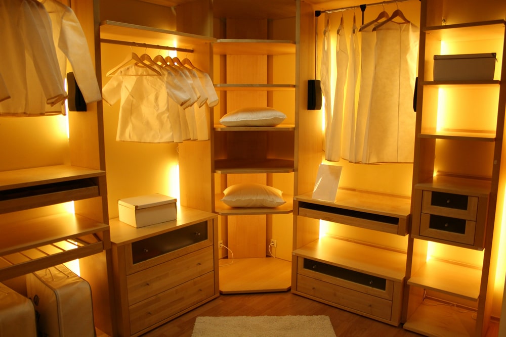 隐藏在木质橱柜中的剥离灯发出的环境光为这个步入式衣柜带来了温暖的氛围，米黄色的墙壁和硬木地板覆盖着蓬松的地毯。