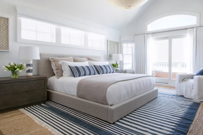 充足的自然光线流动通过这个主卧室的玻璃与分层的地毯和米色平台面临的一个白色的扶手椅床两侧深色木质床头柜和时尚的台灯。