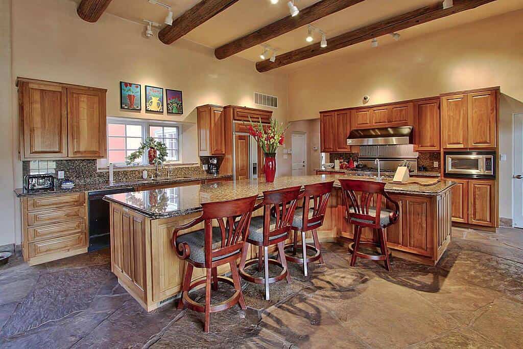 这间可爱的厨房配有米色墙壁和米色天花板，露出木质日志梁。这与L形厨房岛上使用的较轻的木材和Peninsulas搭配很好的木材搭配良好，而是由灰色石材纹理地板和早餐吧的红木大瀑布。