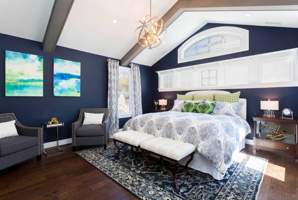 球形吊灯挂在教堂天花板上照亮这个主卧室提供一个客厅和一个舒适的床上,坐在一个经典的宽板地板面积地毯。它周围是深蓝色的墙上安装与抽象绘画。