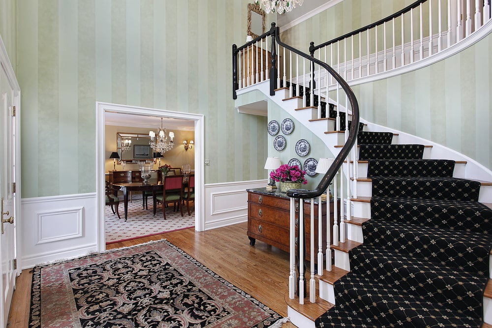乡村风格的门厅，带有弧形楼梯，大面积地毯和绿色室内壁纸。