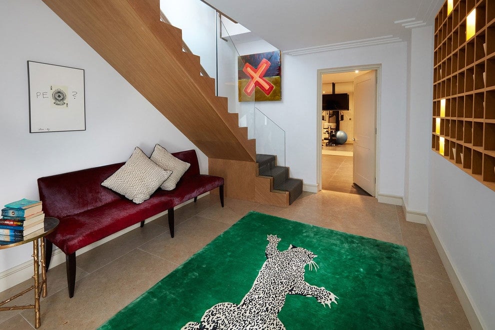 白色的门厅里铺着绿色的地毯，上面有豹纹图案，木制楼梯下面有红色的天鹅绒长椅。在瓷砖地板上有一个圆形的边桌。