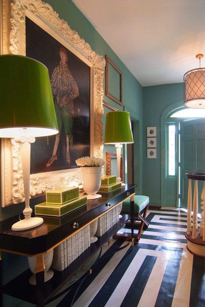 引人注目的黑白花纹地板增加了门厅的特色，设有大型肖像和光滑的控制台桌子，顶部有高大的台灯。旁边有一个带软垫的凳子，与绿色的墙壁融为一体。