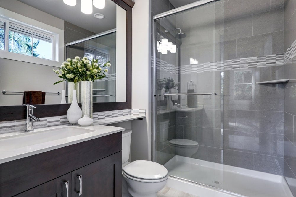 步入式淋浴间的玻璃推拉门上反射的玻璃烛台，照亮了厕所旁边的木质镜框镜子和深色木质梳妆台。