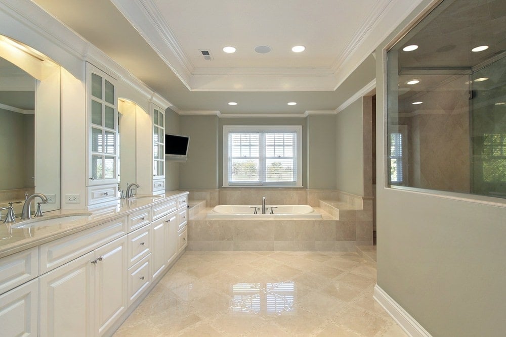 灰色的主浴室里有一间步入式淋浴间和一个巨大的梳妆台，白色框窗边还有一个可随意放置的浴缸。它有米黄色的瓷砖地板，托盘天花板上安装了嵌入式灯。