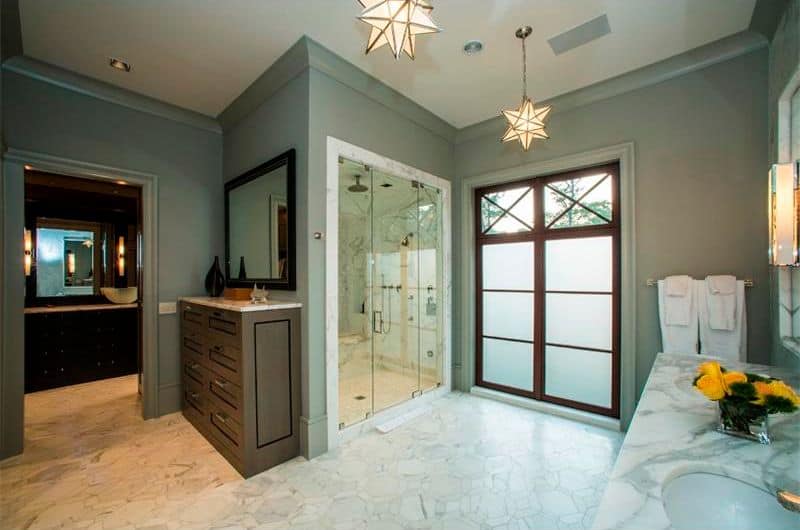 星形吊灯照亮了这间主浴室，展示了木质梳妆台和面向双水槽梳妆台的步入式淋浴间。它有灰色的墙壁，大理石瓷砖地板呈六边形。