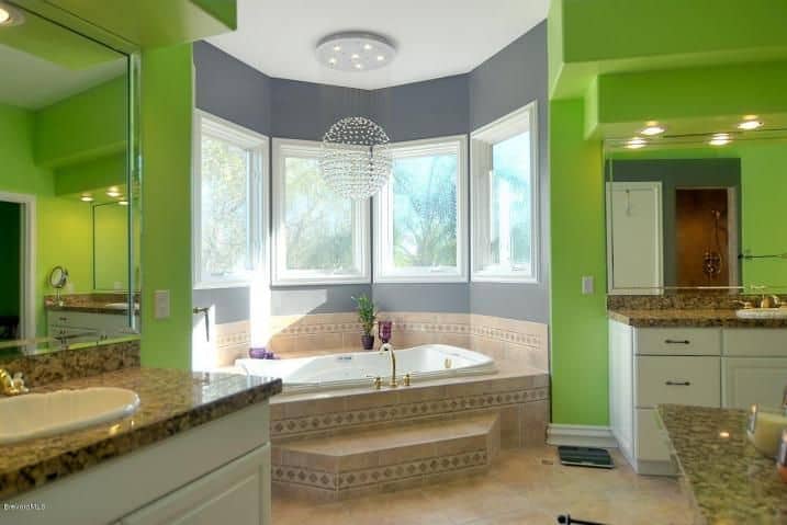 主浴室设有绿色墙壁，设有两个洗手台和一个靠窗的角落浴缸。