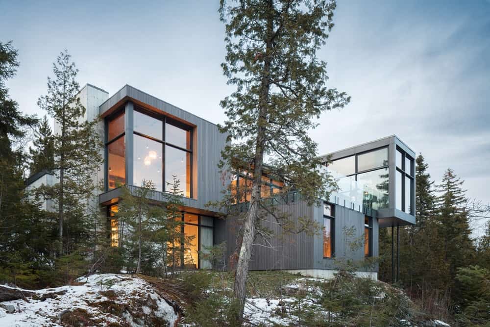现代房子拥有与玻璃窗和门的时髦的外部。周围的环境提供健康的绿色植物，而地球覆盖着雪。