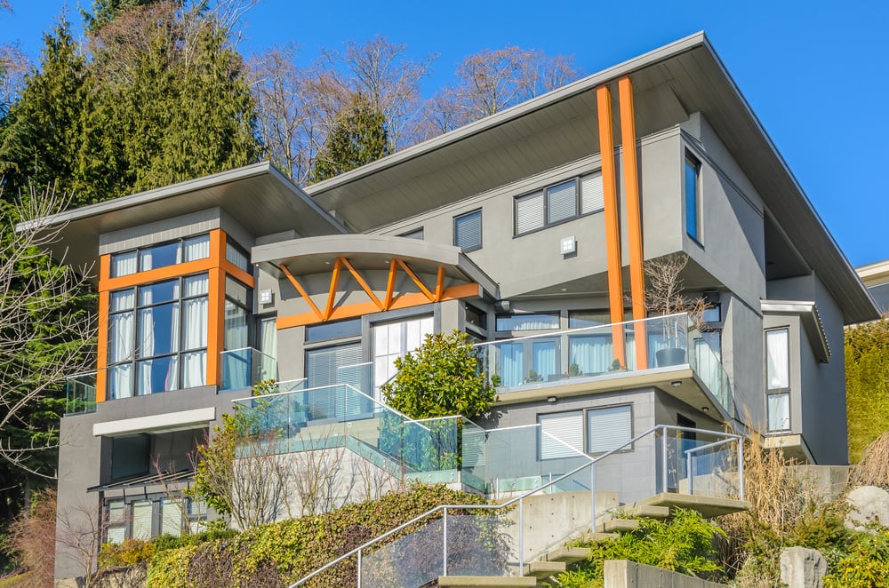 一座现代的房子，灰色的外表带有木头的色调。它的楼梯和阳台上都有玻璃栏杆。它还有一个后院，有一套很好的设施。
