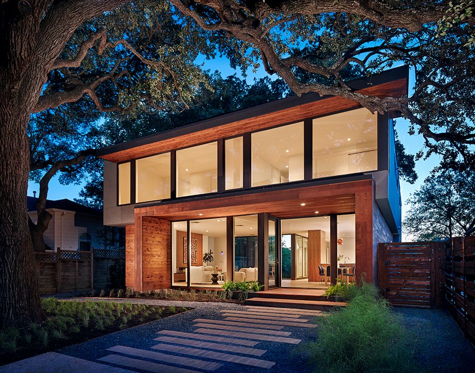 现代住宅拥有木色调的外观和玻璃门窗。它还提供了一个被植物和树木包围的华丽走道。