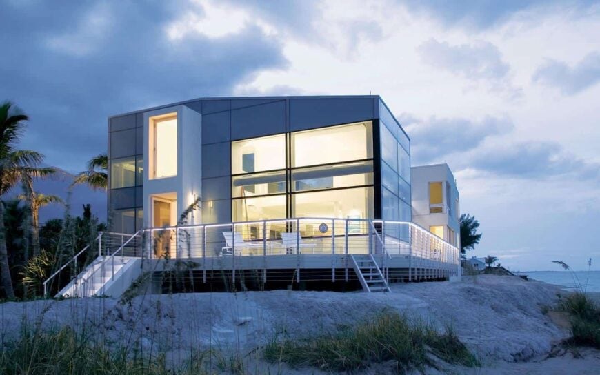 海滩上的一座现代化的大房子，具有令人惊叹的外部设计，有多个大玻璃窗和门。它还有一个带露台的甲板。
