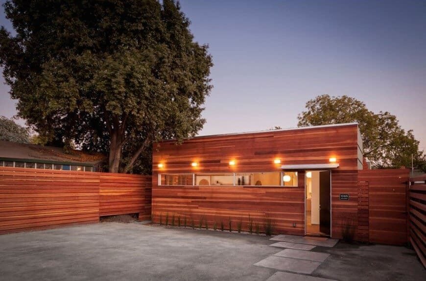 一个现代的房子拥有一个非常有吸引力的木色调外观，温暖的室外照明。它有一个宽阔的后院，带有混凝土地面和一条走道。