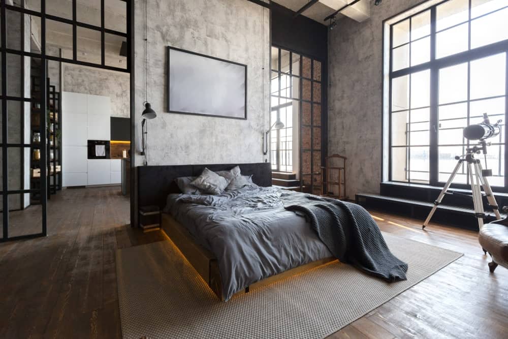 这主卧室与黑色铝框架相匹配的大窗口允许充足的自然光线。它展示一个三脚架落地灯和一个舒适的平台床用温暖的灯光下。