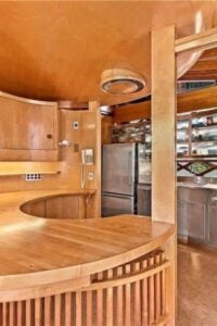定制厨房以圆形房间中的木制橱柜和不锈钢器具为特色，与住宅的整体偏心建筑视觉相匹配。