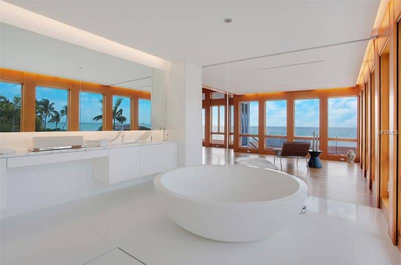 明亮的主浴室,白色的墙壁,白色瓷砖地板和白色的天花板。它有一个浮动的虚荣洗手盆计数器和一个圆形dropin浴缸。房间里也有玻璃窗俯瞰美丽海景。