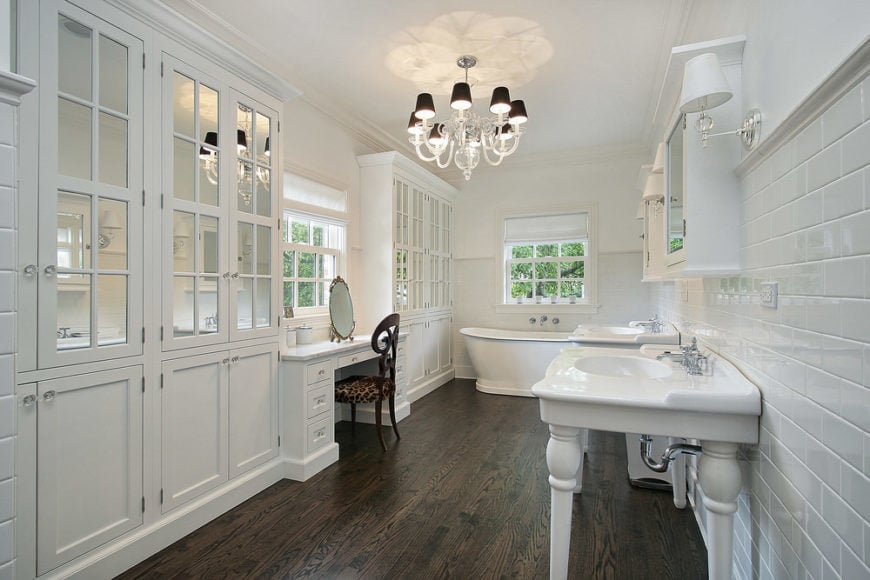 宽敞的主浴室，硬木地板和白墙。它有一个化妆台，两个洗手台和一个独立的浴缸。房间里有一盏别致的枝形吊灯。