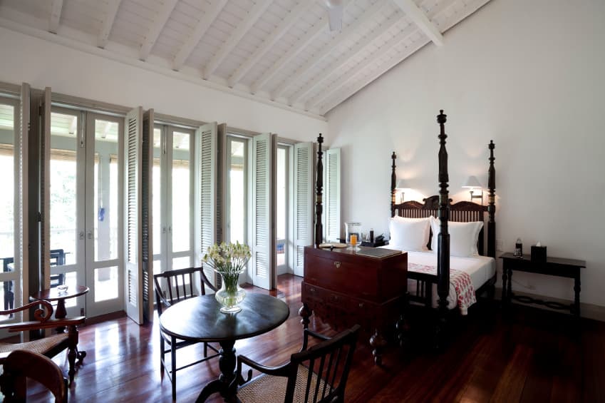 深色硬木地板与白色墙壁和覆盖木板的棚屋天花板形成了鲜明的对比。这个房间有一张天篷床，座位区横跨展示柳条椅子和圆形木桌。