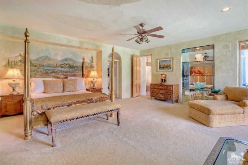 地中海风格的主卧室有一张四柱床，上面有一幅宁静的景观壁画。它包括一个质朴的梳妆台和一个与地毯地板融为一体的米色躺椅。