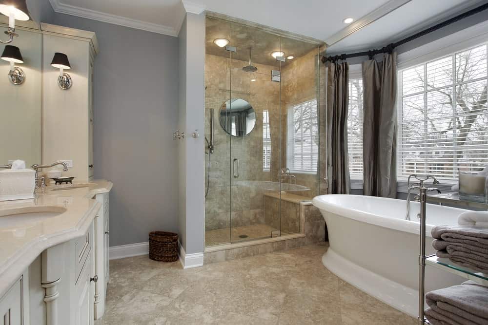中型主浴室设有灰色墙壁和瓷砖地板。这里有一个带两个水槽的洗手台，由壁灯照明，还有一个独立的深泡浴缸和一间步入式淋浴房。