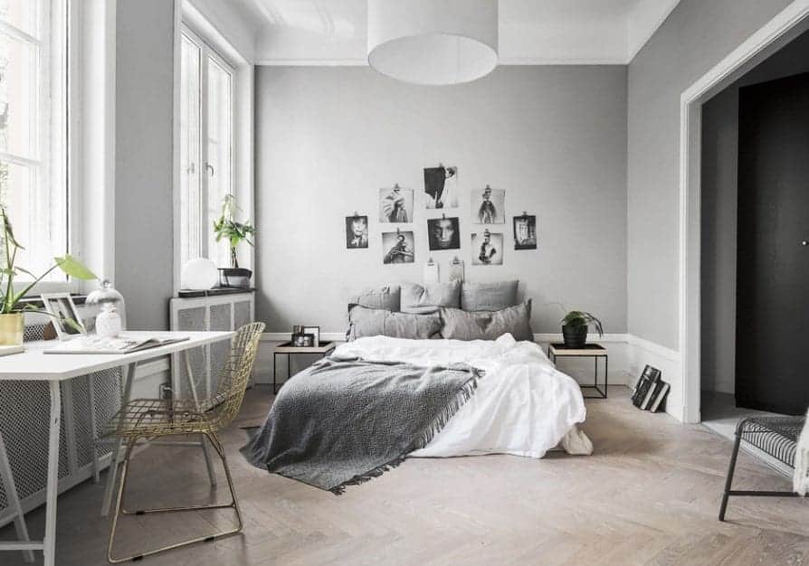 斯堪的纳维亚主卧室有一个舒适的床上人字形木地板和白色搭配了一个多孔的椅子的桌子。装饰着一个相册和绿色盆栽,使精神振作了房间。