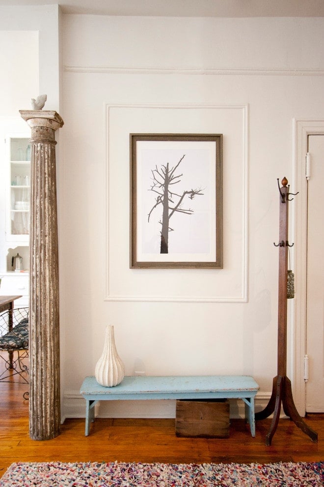 天蓝色的长凳两侧是衣架和破旧的希腊柱子，为门厅带来了色彩。它装饰着彩色地毯，一个华丽的花瓶和一幅用白色镶边框起来的树枝艺术品。