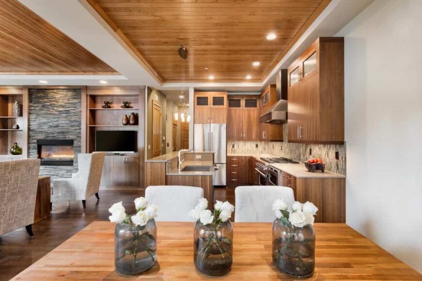 这间餐厅式厨房拥有一个覆盖木板的托盘天花板。它与木制橱柜和矩形餐桌搭配白色软垫椅子很好地融合在一起。