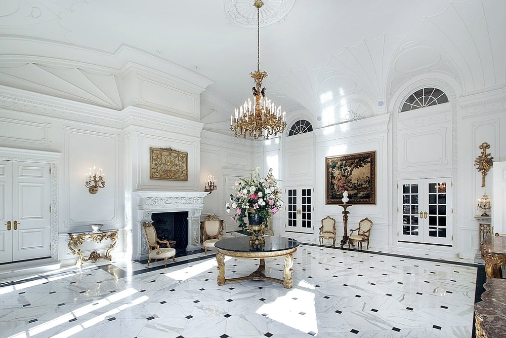 豪华的门厅拥有一个宏伟的镀金吊灯挂在一个圆形的中心桌子，上面有一个华丽的花瓶。它周围是优雅的控制台桌椅，法式门和壁炉两侧的蜡烛烛台。