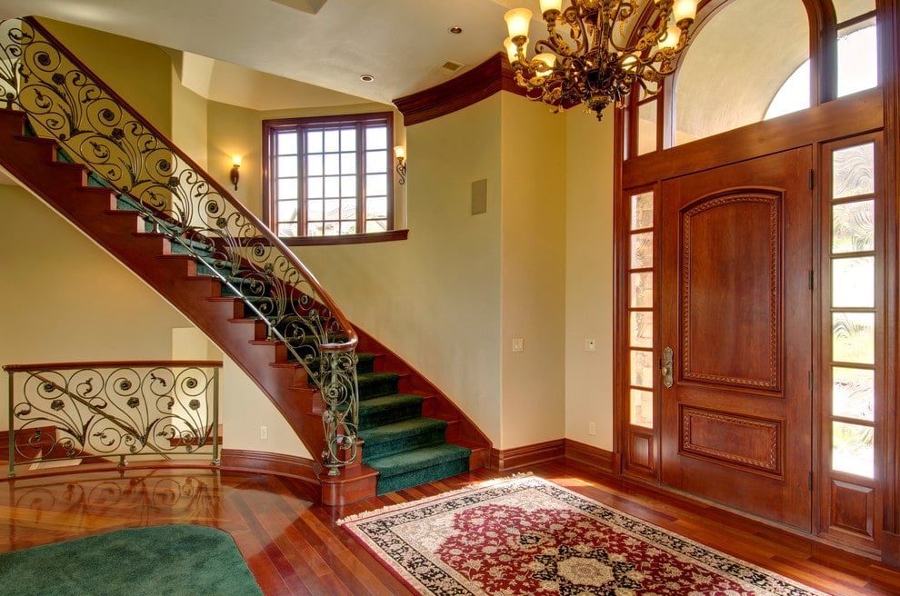装饰着绿色天鹅绒地毯的华丽楼梯在这个经典的门厅中增加了陈述，温暖的吊灯和木制前门与抛光的硬木地板融为一体，上面有绿色和红色的印花地毯。