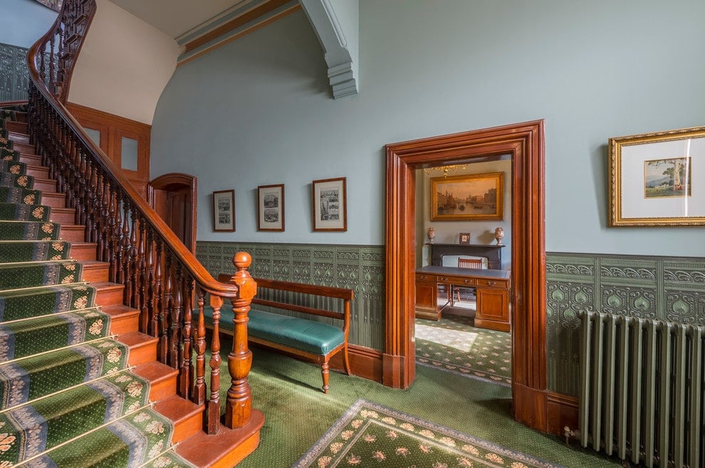 维多利亚风格的门厅里摆满了装裱好的艺术品，有软垫的长凳贴着有纹理的墙纸。它有柔软的蓝色上层墙壁和绿色地毯地板，与木楼梯上的跑步器相匹配。