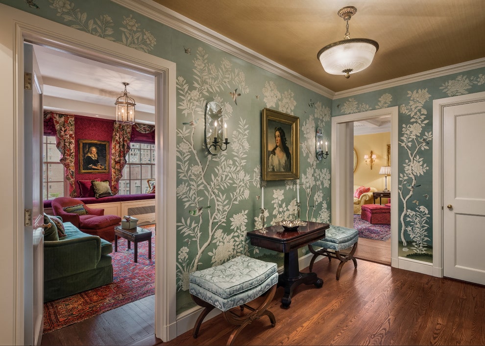 经典的门厅覆盖着绿色墙纸，由华丽的肖像装饰。它配有深色木边桌和天然硬木地板上的软垫凳子。