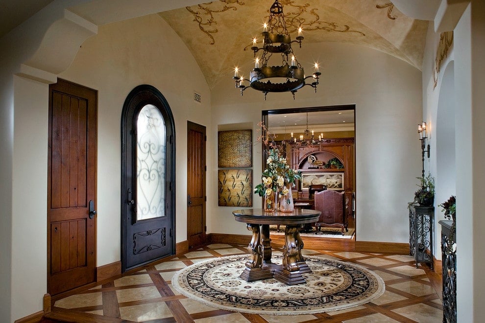 维多利亚风格的门厅被悬挂在拱顶天花板上的两层枝形吊灯照亮。它有一个拱形的前门和一个圆形的中心桌子，桌子放在有图案的地板上的流苏地毯上。