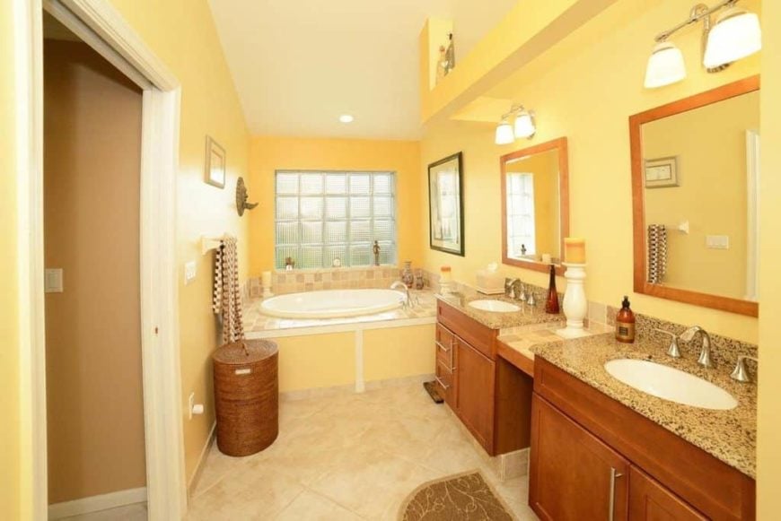 主浴室有黄色墙壁和棚顶天花板，以及瓷砖地板。它的一侧有一个插入式浴缸，还有一个步入式淋浴间和两个带大理石台面的水槽柜台。