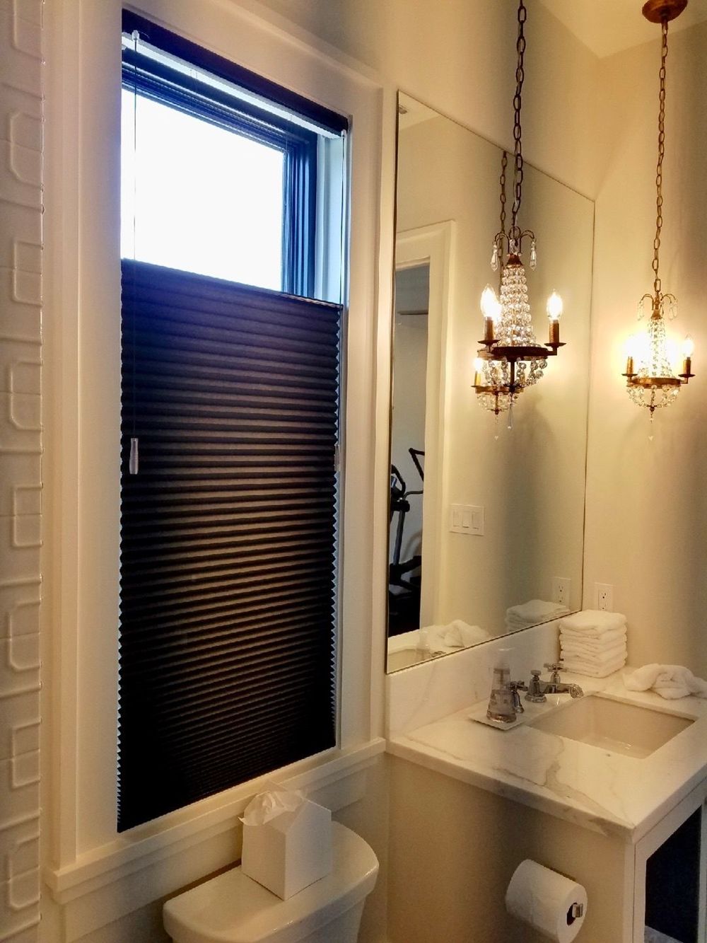 这间主浴室设有一个小的单水槽，由一对华丽的枝形吊灯悬挂在高高的天花板上照明。
