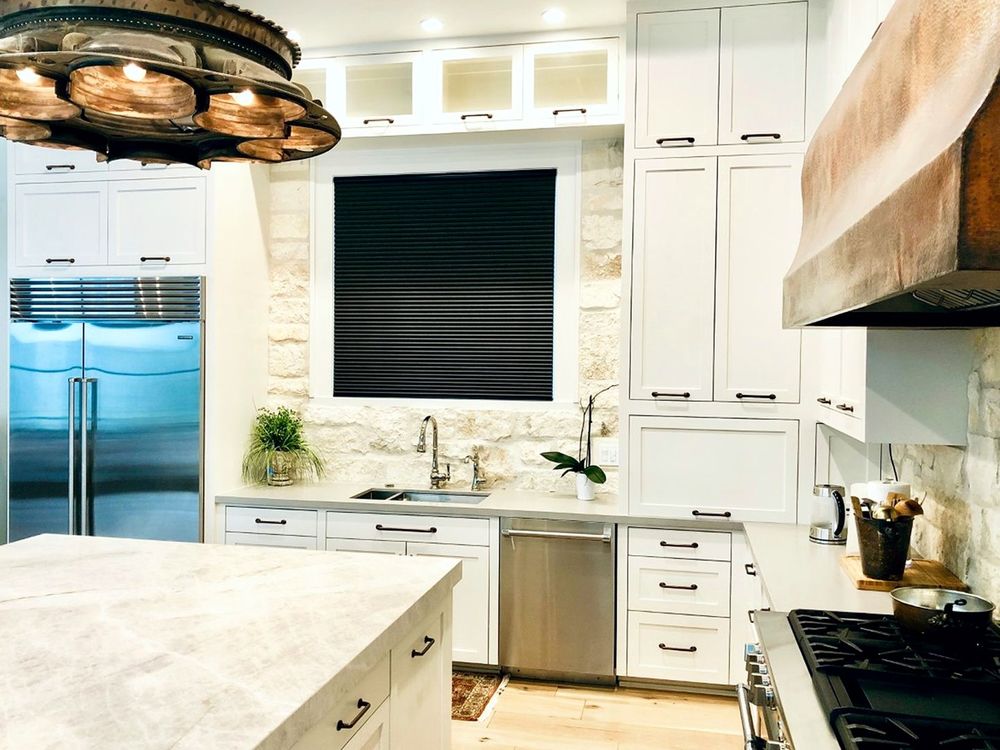 这间厨房拥有白色橱柜和l型厨房台面，以及一个带大理石台面的大型中央岛台。