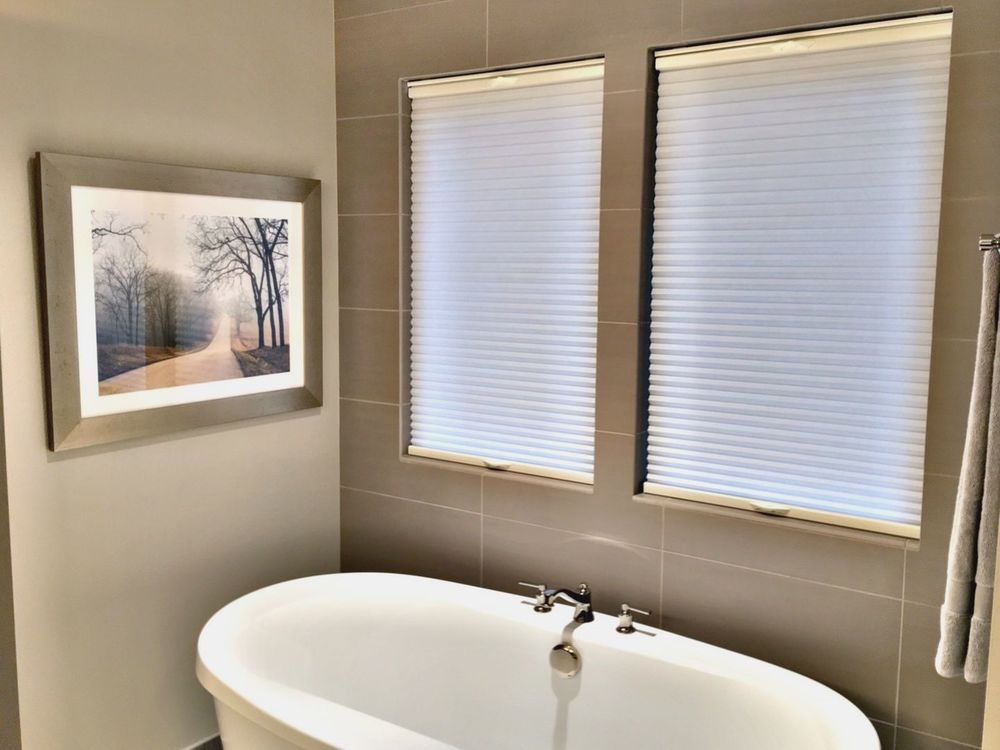 一间带瓷砖墙和独立浴缸的主浴室，以及带遮阳板的窗户。